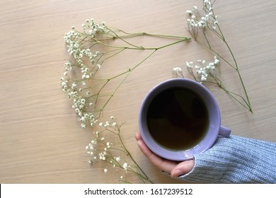 Unrecognizable person in a cozy sweater holding a cup of tea, with gypsophila flowers on wooden table. Flat lay.  - Powered by Shutterstock