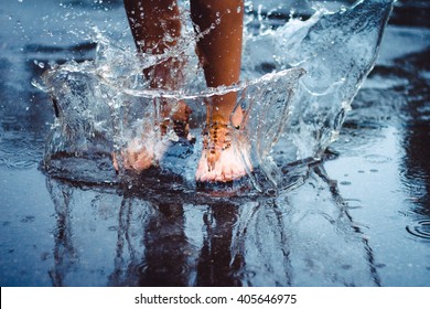 Unrecognizable person (female) is splashing water in a puddle on a rainy day in the city. Legs in puddle.