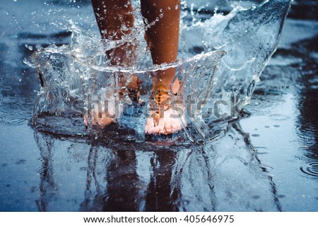 Unrecognizable person (female) is splashing water in a puddle on a rainy day in the city. Legs in puddle.