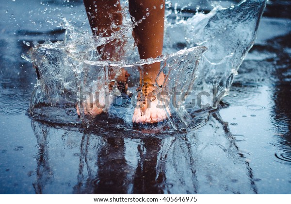 Unrecognizable person (female)\
is splashing water in a puddle on a rainy day in the city. Legs in\
puddle.