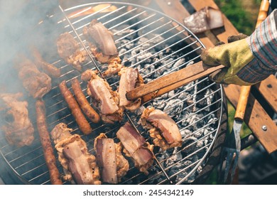 Unrecognizable person making barbecue on the grill outdoors. Unknown male or female grilling bacon and sausages outdoors. - Powered by Shutterstock