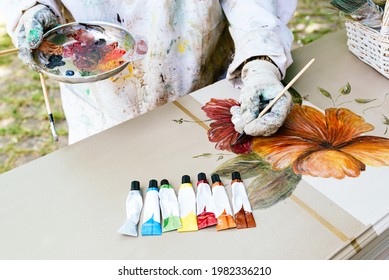 Unrecognizable Person Painting Flowers With A Brush On An Old Wooden Furniture. Artist Using His Color Palette With Various Acrylic Paints On A Wooden Table.