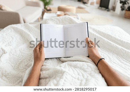 Unrecognizable Person Reading Journal While Relaxing In Bed At Home, Cozy Setting