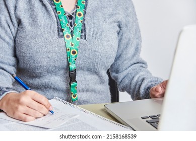 Unrecognizable Person Takes Notes While Studying Or Working At Home, Using A Sunflower Lanyard, Symbol Of People With Invisible Or Hidden Disabilities.