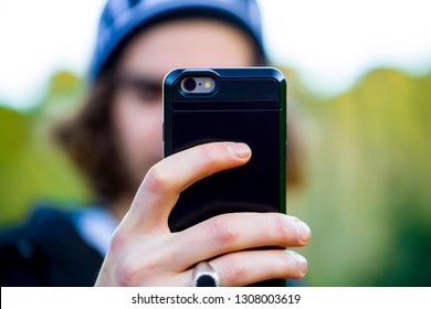 Unrecognizable Person Taking A Selfie Photo With His Smartphone. Close Up On The Back Of A Mobile Phone In A Black Case.