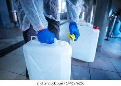 Unrecognizable person technologist in white protective suit handling acid or detergent in chemical industry. Industrial worker opening plastic canister to use chemicals.