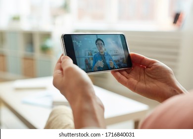 Unrecognizable person watching Asian man speaking while having online meeting on smartphone, horizontal close-up shot