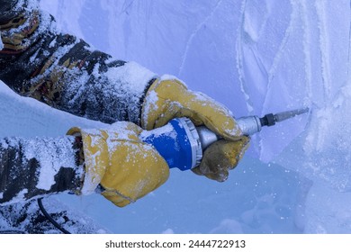 Unrecognizable person wearing yellow leather winter gloves using a power tool to carve a large block of ice. - Powered by Shutterstock