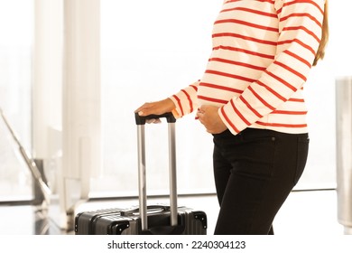 Unrecognizable pregnant caucasian woman with baggagein airport waiting for check-in registration.Safe flying, travelling during pregnancy concept. Copy space. - Shutterstock ID 2240304123