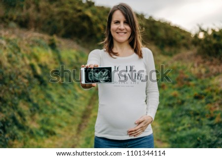 Unrecognizable pregnant woman showing ultrasound of her baby on the mobile