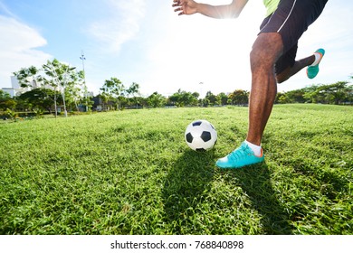 Unrecognizable professional soccer player running after ball and preparing to kick it while having training on football field
