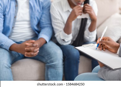 Unrecognizable psychologist taking notes about young black couple's problems on marital therapy session in office