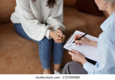 Unrecognizable Psychologist Talking With Female Client Taking Notes During Psychotherapy Session Sitting In Office. Selective Focus, Cropped