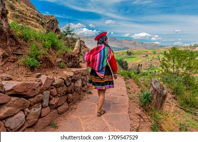 Unrecognizable Quechua Indigenous Woman in traditional clothes walking along ancient Inca Wall in the ruin of Tipon, Cusco, Peru.