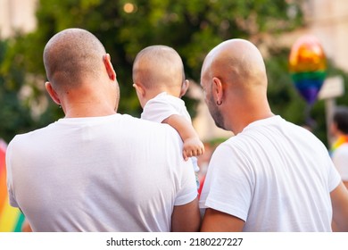 Unrecognizable Real People From Behind At Pride Parade, Support For LGBTQIA Community. Two Gay Fathers With Child From Behind. Gay Family. Crowd Of People At Public Event. Lgbtq+  Parents.