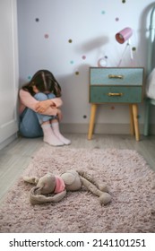 Unrecognizable Sad Little Girl Sitting On The Floor Of Her Bedroom With Stuffed Toy Lying. Selective Focus On Stuffed Toy In Foreground