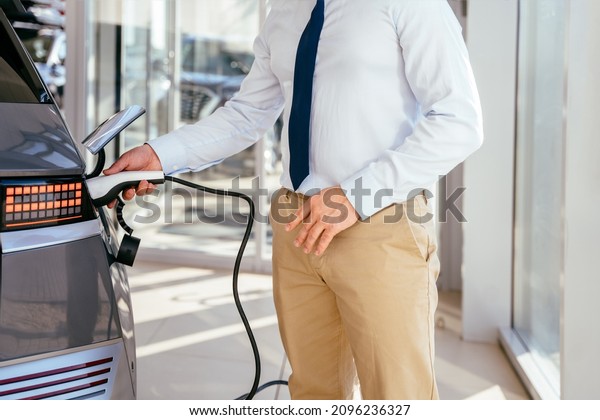 Unrecognizable sales man\
charging modern eco-friendly vehicle with the power cable supply\
plugged in. Customer buying first electric car in the showroom. Eco\
car sale\
concept.