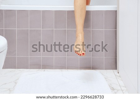 Unrecognizable senior woman has finished taking shower and is stepping over edge of bathtub