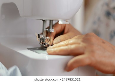 Unrecognizable senior woman sewing with a close-up view of her hands guiding fabric through a sewing machine. Concept of sewing craftsmanship - Powered by Shutterstock