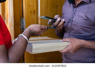 unrecognizable shot of customer paying delivery boy by scanning qr code on mobile phone at door - concept of contectless or cashless payment,technology and shipment service.