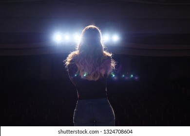 unrecognizable singer standing on stage at microphone in night club, back view