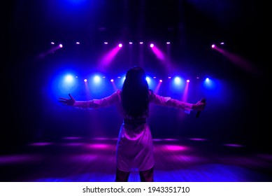 Unrecognizable singer standing on stage at microphone, back view, neon lights