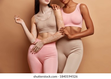 Unrecognizable slim women embrace and demonstrate perfect body dressed in comfortable tops and leggings have different skins. Multicultural lesbian ladies