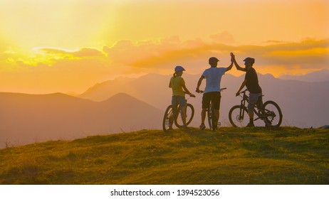 Unrecognizable sporty tourists high five after a successful evening bike ride in the golden lit mountains. Three cross country cyclists celebrate at sunset after a successful mountain biking adventure - Powered by Shutterstock