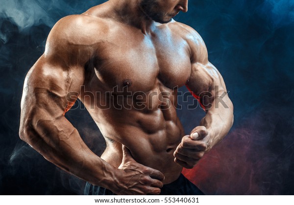 Unrecognizable Strong bald bodybuilder with six pack. Bodybuilder man with perfect abs, shoulders,biceps, triceps and chest, personal fitness trainer flexing his muscles in blue, red smoke