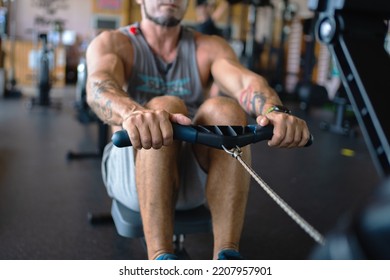 Unrecognizable strong man rowing using a machine in a gym