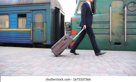 Unrecognizable Successful Businessman In Black Formal Suit Walking Along Platform Near Passing Train. Young Confident Man With His Luggage Going On Business Trip. Stylish Man Stepping Outdoor. Slow Mo