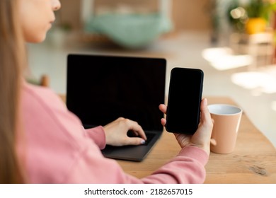 Unrecognizable Teen Girl Holding Smartphone With Blank Screen For Mockup Template, Sitting At Table With Laptop Computer With Empty Screen, Copy Space