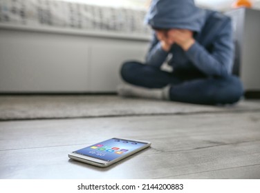 Unrecognizable teenager boy crying desperate for bullying with mobile lying on the floor in foreground. Selective focus on mobile in foreground - Powered by Shutterstock