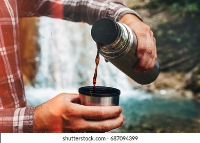 Unrecognizable Traveler Pouring Tea Or Coffee To Cup From Thermos On Waterfall Background. Tourism And Travel Concept - Powered by Shutterstock