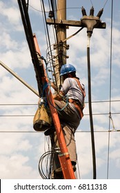 Unrecognizable Utility Worker (shot Sideways) On Top Of A Ladder With Electrical Cables And Post In The Background.