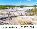 Unrecognizable visitors walking on the Porcelain Basin boardwalk trail surrounded by geothermal pools inside Norris Geyser Basin of Yellowstone National Park, Wyoming, USA.