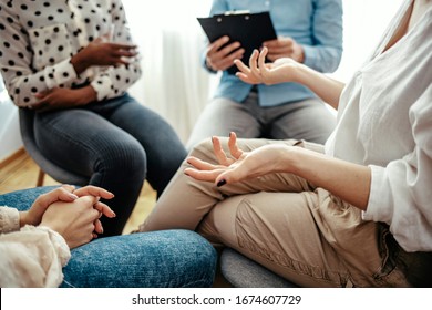 Unrecognizable Vulnerable Woman Participates In Group Therapy Session. Unrecognizable Caucasian Person Gestures While Speaking. Group Of People Sitting In A Circle During Therapy. 