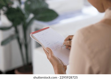 Unrecognizable waitress writes orders in notepad, close up rearview over female shoulder. Woman makes notes, jotting information in notebook, planning tasks, working or studying standing alone indoors - Powered by Shutterstock