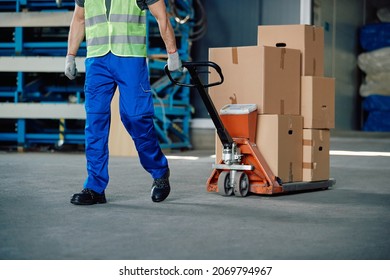 Unrecognizable warehouse worker pulling packages on pallet jack at storage compartment. Copy space. - Powered by Shutterstock