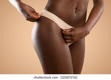 Unrecognizable well fit young black woman posing in nude panties, showing hairless bikini line or smooth sexy hips without cellulite and stretch marks, isolated, studio background, copy space
