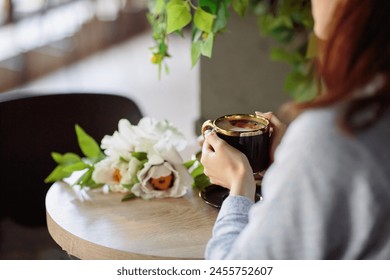 Unrecognizable woman in blue dress sitting at table with flowers and enjoying cup of coffee and croissant in cafe. - Powered by Shutterstock