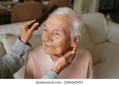 Unrecognizable woman brushing elderly lady's hair with a comb. Granddaughter helping granny with a haircut. Family values concept. lose up, copy space, background. - Powered by Shutterstock