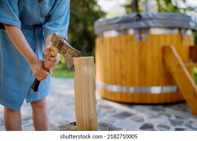 Unrecognizable woman chopping wood preparing it for for wooden bathtub with a fireplace to burn wood and heat water in backyard in mountains. - Powered by Shutterstock