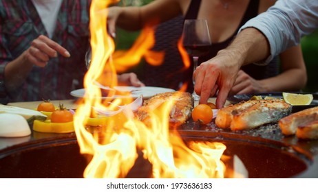 Unrecognizable woman cooking bbq food on fire flame for grill party outdoors. Closeup unknown woman putting vegetables on bbq grill outside. Happy guys grilling dinner on backyard.
