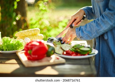 Unrecognizable woman cutting fresh eggplant vegetables on wooden board during weekend barbecue in yard, outdoor, prepare for grilling, summer family picnic, food on the nature.
