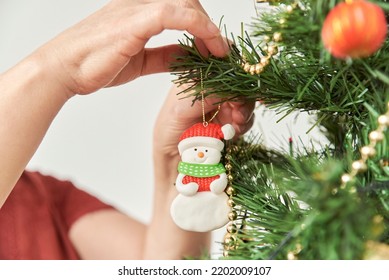 Unrecognizable woman decorating a Christmas tree at home, close up of the hands hanging a snowman ornament on a branch. - Powered by Shutterstock