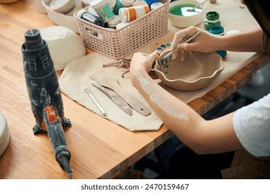 Unrecognizable woman decorating dishware bowl in pottery workshop - Powered by Shutterstock