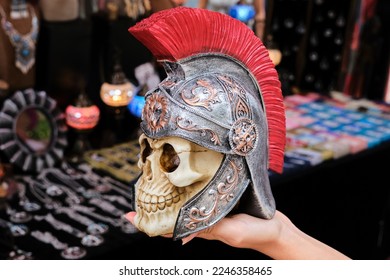Unrecognizable woman demonstrating fake scull of Roman centurion in galea against stall with souvenir on market - Shutterstock ID 2246358465