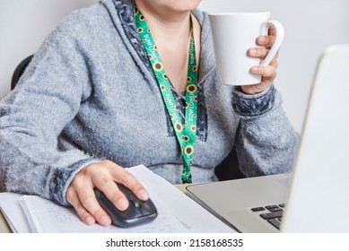 Unrecognizable Woman Drinking A Cup Of Coffee While Studying Or Working At Home, Using A Sunflower Lanyard, Symbol Of People With Invisible Or Hidden Disabilities.