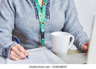 Unrecognizable Woman Drinking A Cup Of Coffee While Studying Or Working At Home, Using A Sunflower Lanyard, Symbol Of People With Invisible Or Hidden Disabilities.